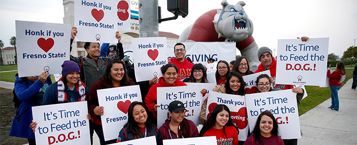 Fresno State student volunteers on one of the campus corners holding up Day of Giving signs