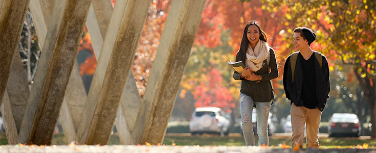 Two students walking by the Sweet Sixteen Monument near the Conley Art Building at Fresno State